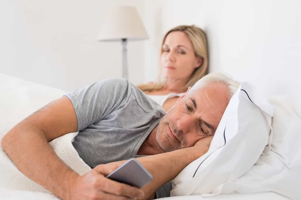 A white male and female couple in their 50s lying in bed but very apart, looking distanced and unhappy