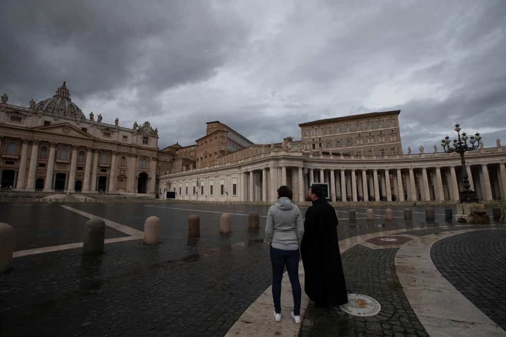 Two people stand in an empty St Peter’s Square, at the Vatican as Pope Francis recites the Angelus noon prayer in his studio