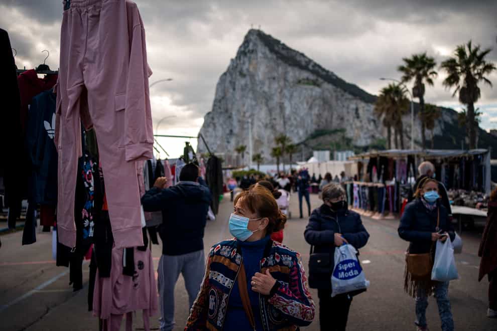 Backdropped by the Gibraltar rock, people wearing face masks walk along the stalls of a weekly market at the Spanish city of La Linea (Emilio Morenatti/AP)