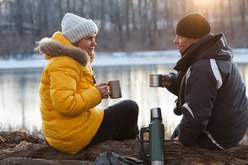 Couple drinking hot coffee or tea from a thermos flask and sitting next to stunning winter landscape