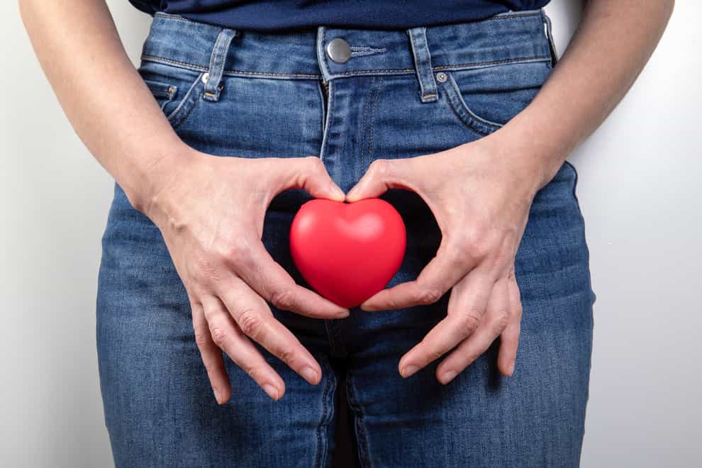 Close up of a woman holding a small red heart in front of her pelvic area