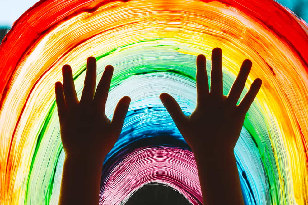 Children's hands in front of a painted rainbow