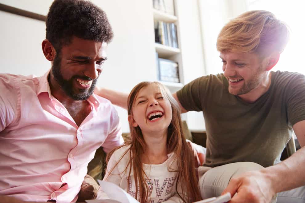 Interracial gay male couple sitting with their young daughter, laughing