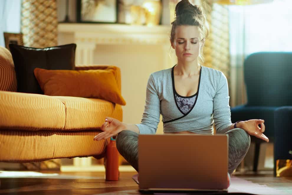 woman meditating using online streaming yoga site in laptop