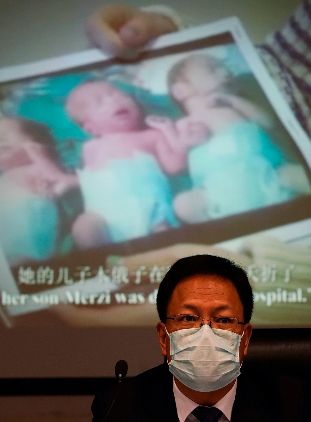 Xu Guixiang, a deputy spokesperson for the Xinjiang regional government, looks up near a slide showing a photo of Uighur infants during a press conference (Ng Han Guan/AP)