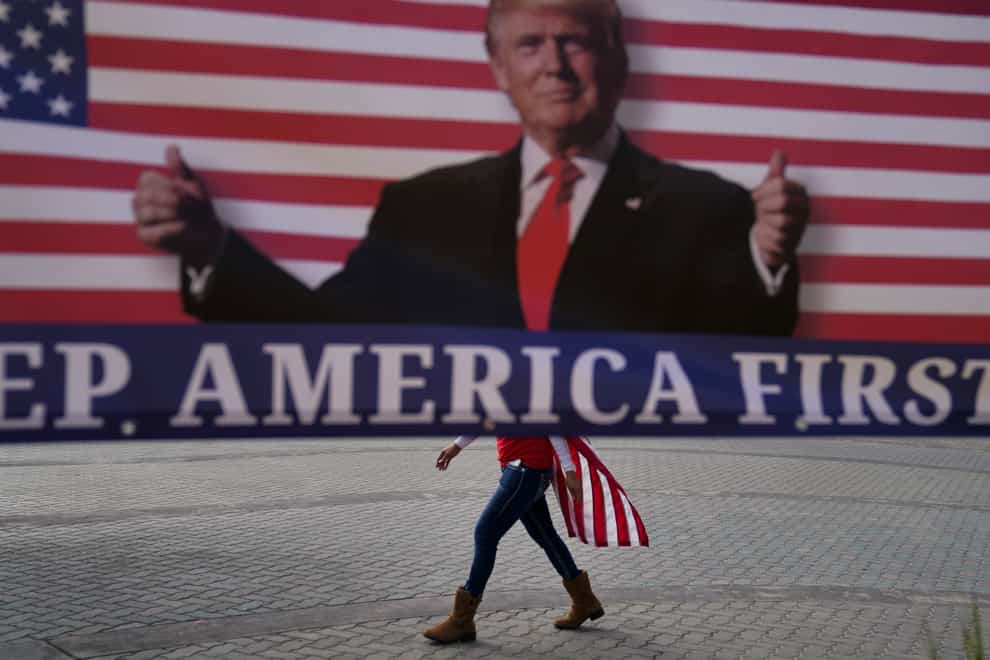A woman draped in an American flag walks past a banner supporting President Donald Trump (Jae C. Hong/AP)