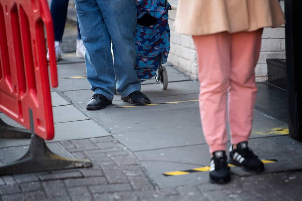 Customers queue between social distancing markers on the pavement outside a supermarket