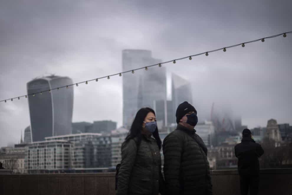 A couple wearing face masks walk past a view of the City of London