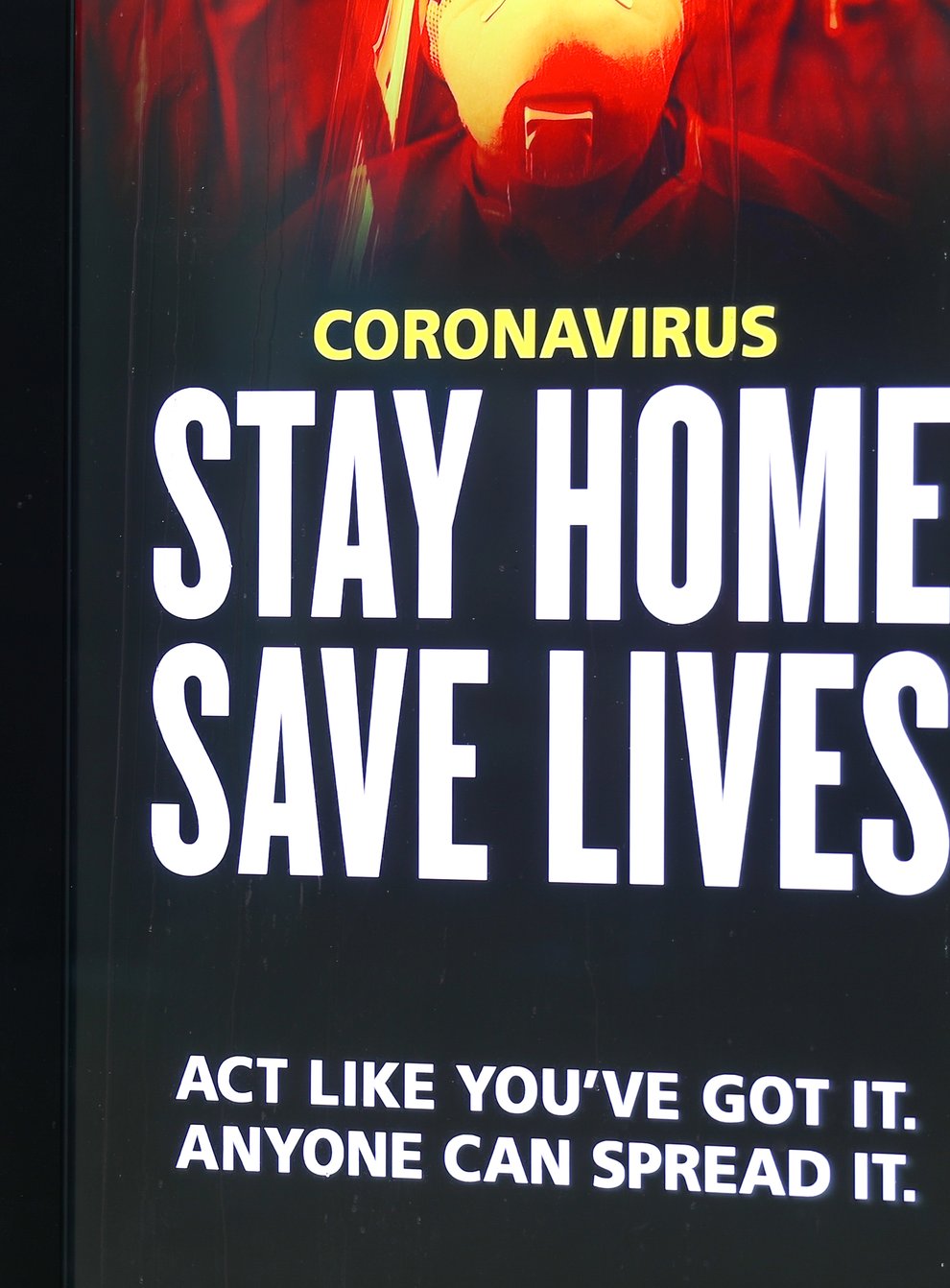 A person walks past a Stay Home, Save Lives sign