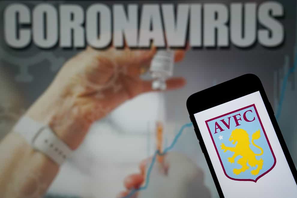 Aston Villa Football Club logo seen displayed on a mobile phone with a coronavirus illustration on a monitor in the background