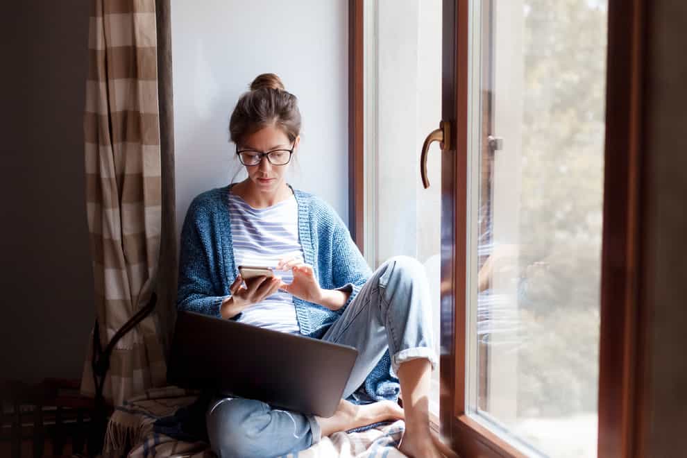 Young woman alone at home using mobile and laptop.