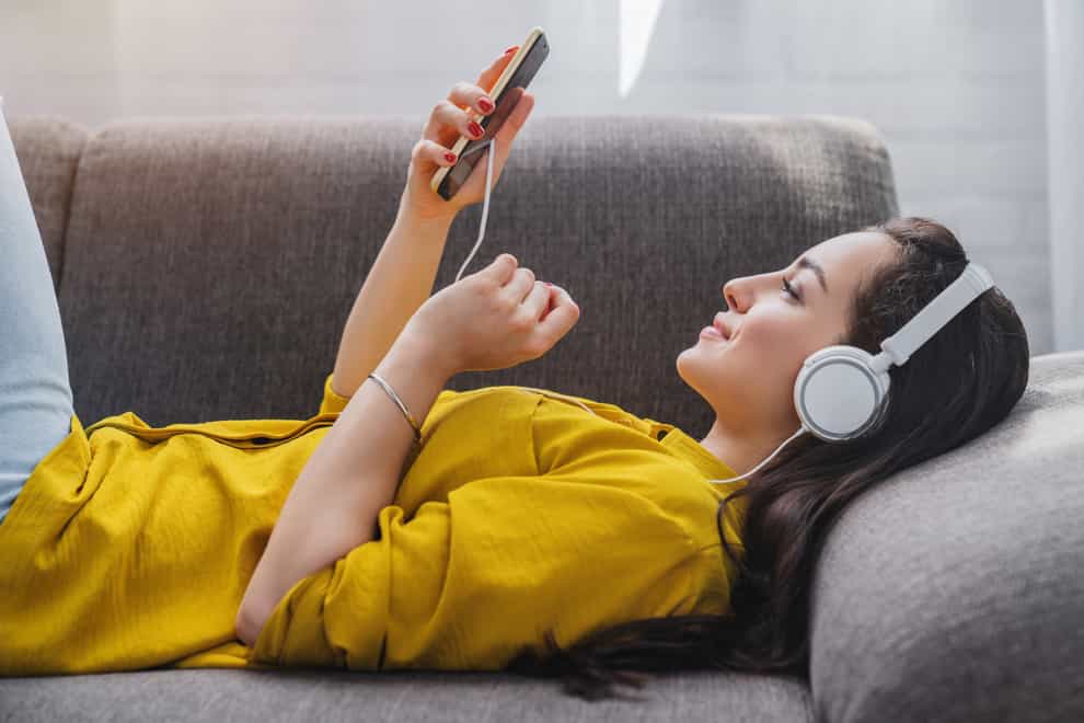Young woman lying on a sofa with headphones on