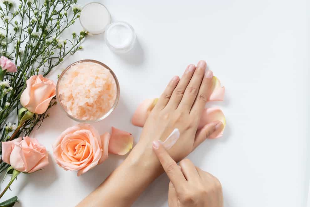 woman apply white cream on her hands on white background with jar of cosmetic cream, salt spa scrub ,rose and white flowers with copy space