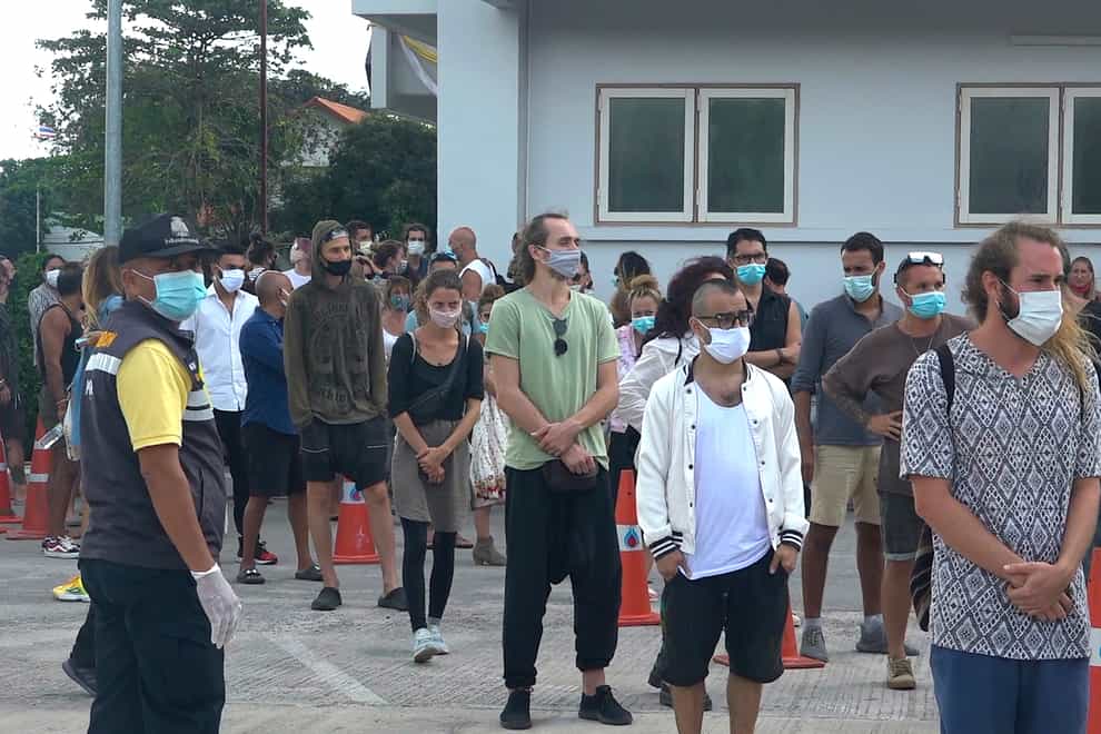 An immigration officer stand beside a group of people in front of police station attending a court hearing through video conferencing on Koh Phangan island