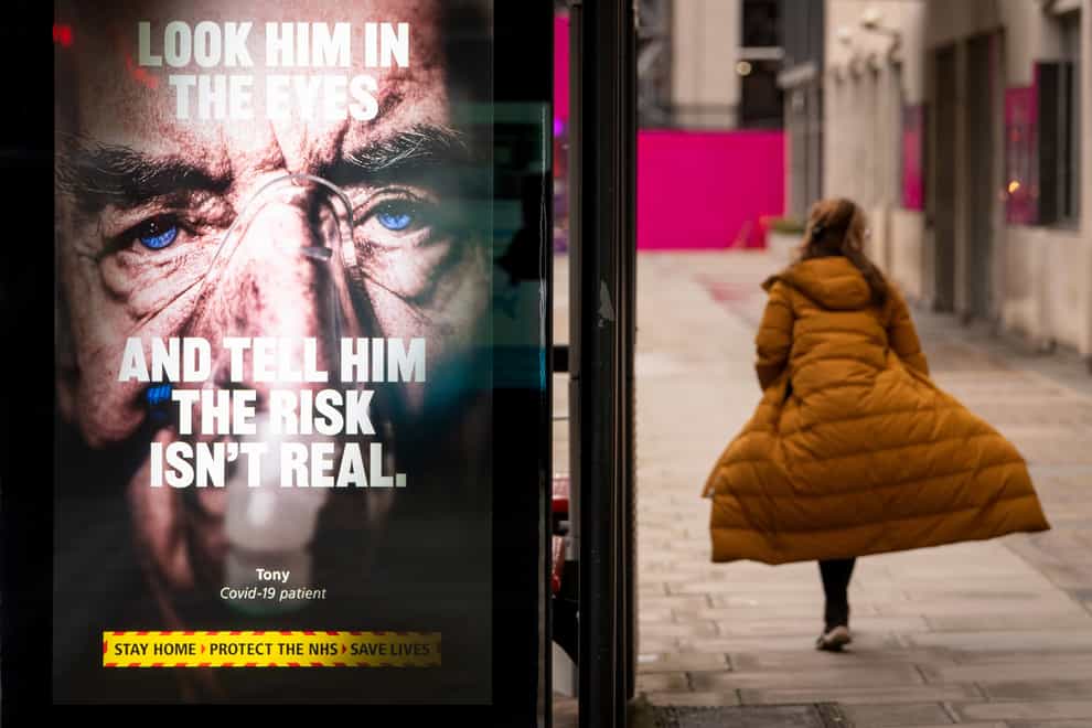 A woman passes a Government coronavirus advert in a bus shelter in central London
