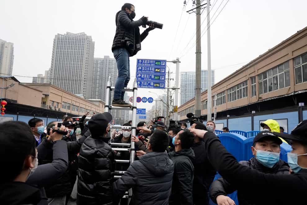 A photographer on a ladder tries to take photos of the World Health Organisation convoy after it entered Huanan Seafood Market on the third day of a field visit in Wuhan in central China’s Hubei province