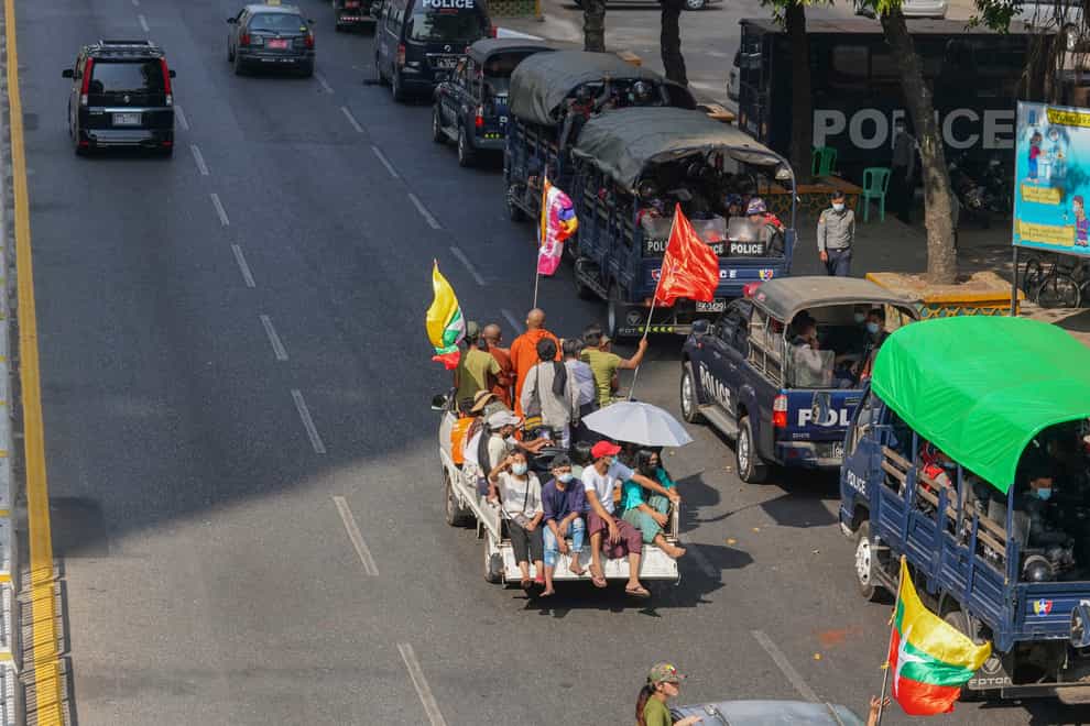 A vehicle with Myanmar and military flags and supporters of the Myanmar military and the military-backed Union Solidarity and Development Party passes by a row of police vehicles with police security onboard parked near the Kyauktada police station in Yangon, Myanmar (AP)