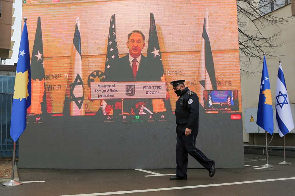 A Kosovo police officer in Pristina walks by a screen displaying a virtual signing ceremony address by Israeli foreign minister Gabriel Ashkenazi (Visar Kryeziu/AP)
