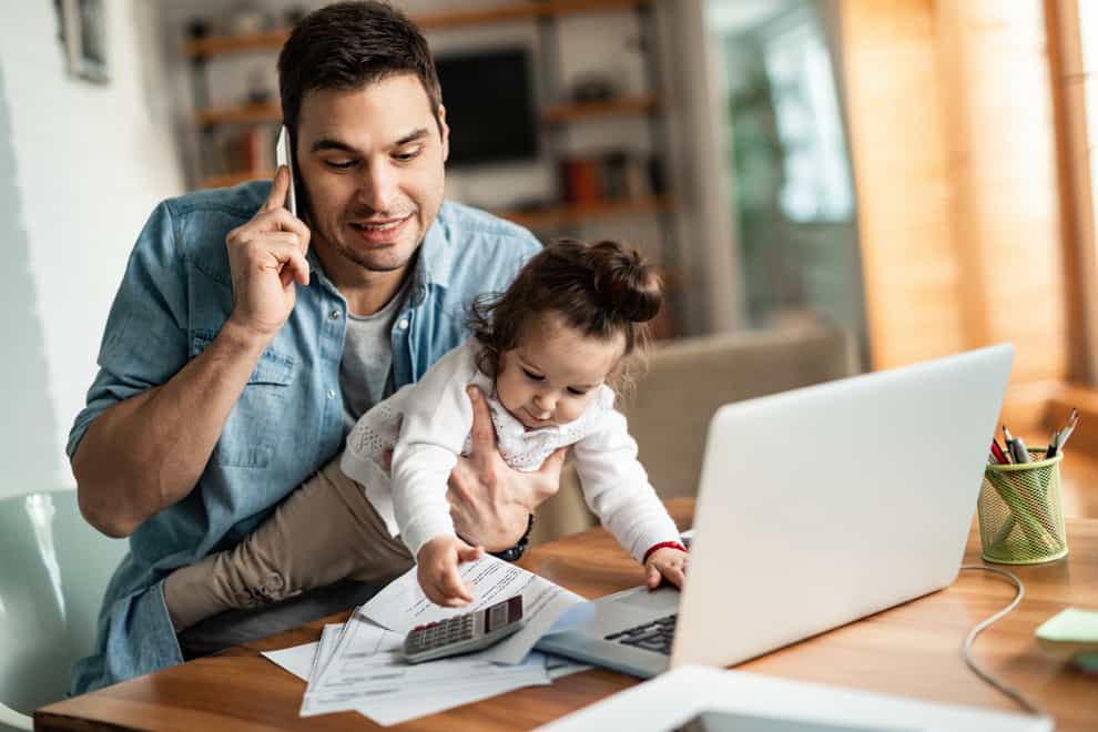 Young working father talking on the phone while holding his daughter (iStock/PA)