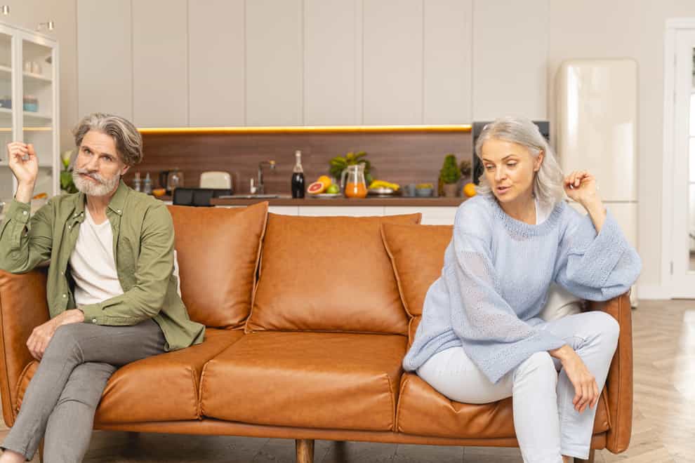 Unhappy married couple sitting at opposite ends of a sofa