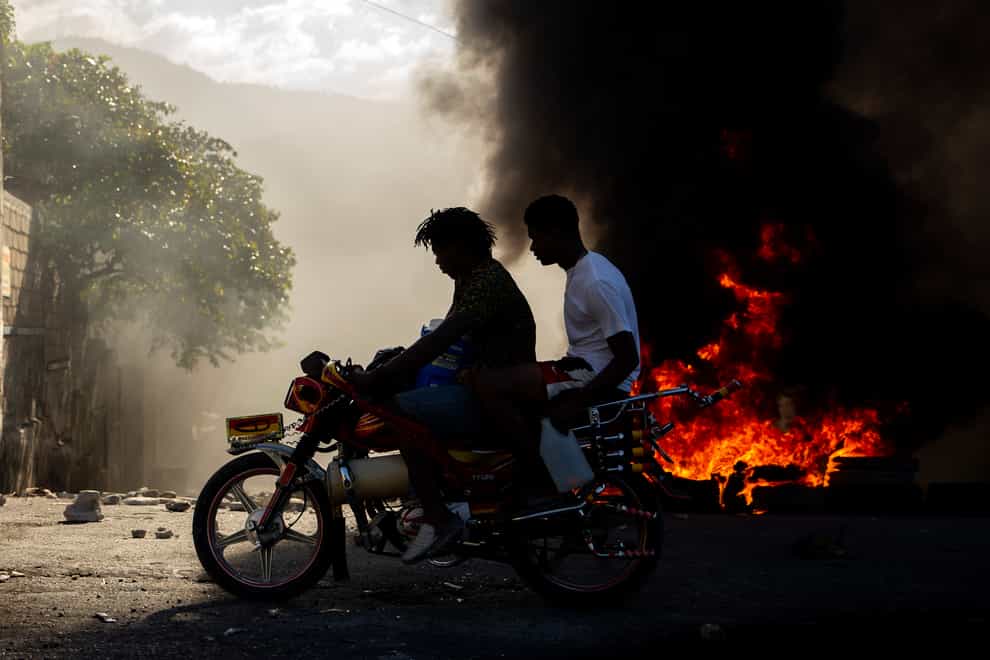 Men ride a motorcycle past a burning barricade during a protest to demand the resignation of Haitian President Jovenel Moise in Port-au-Prince, Haiti (Dieu Nallo Chery/AP)