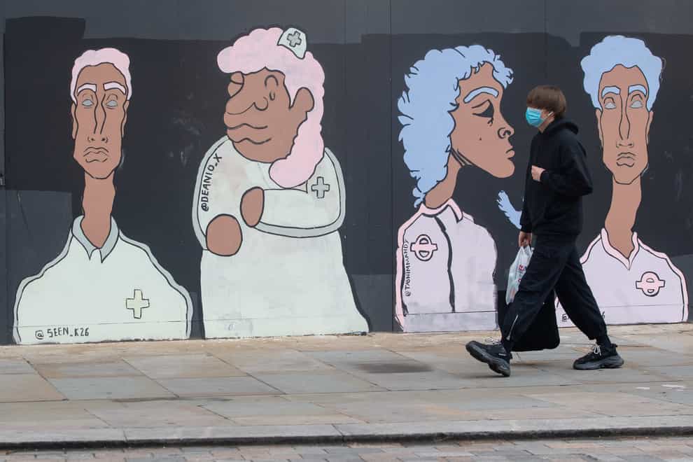 A man wearing a protective face mask passes a mural showing Bame medical and transport workers
