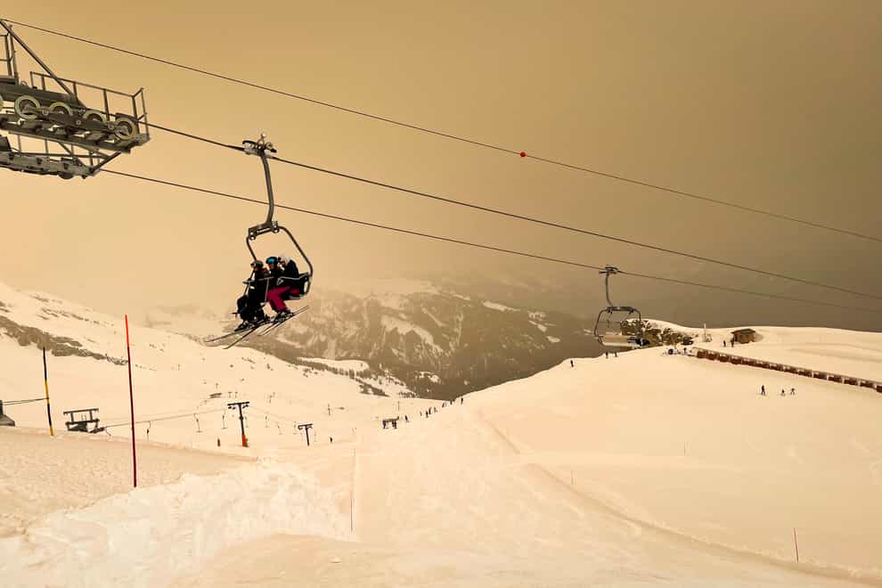 Skiers wearing protective face masks sit on a chairlift as Sahara sand colours the snow and the sky in orange and creates a special light atmosphere in the Alpine resort of Anzere, Switzerland