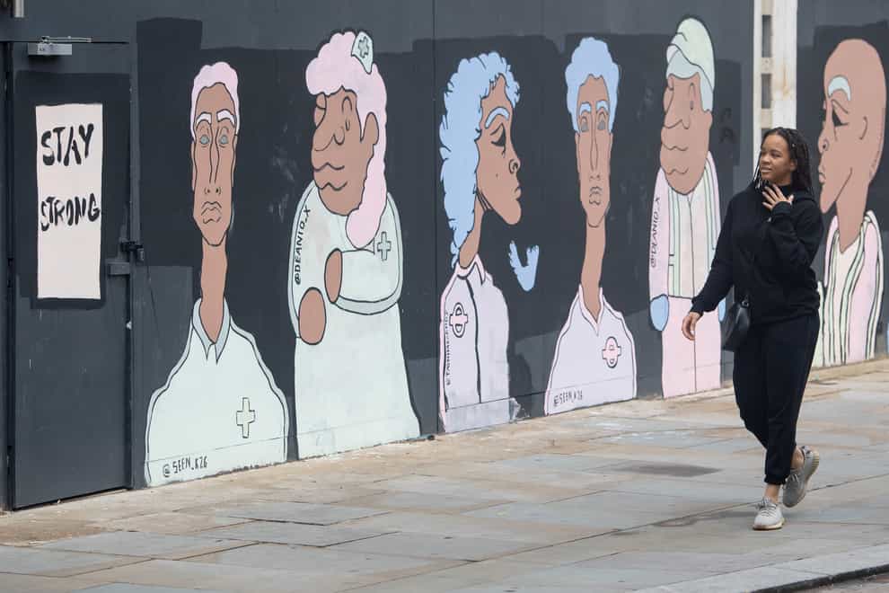 A woman passes a mural depicting BAME workers