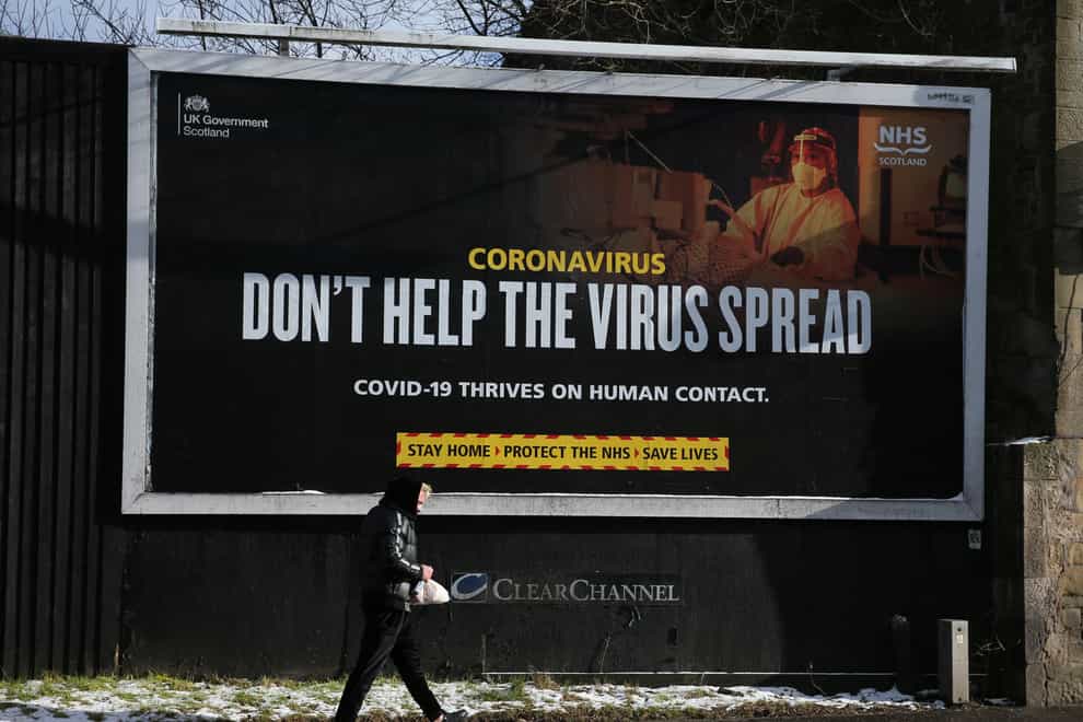 A person walks passed a Coronavirus related advert on a billboard