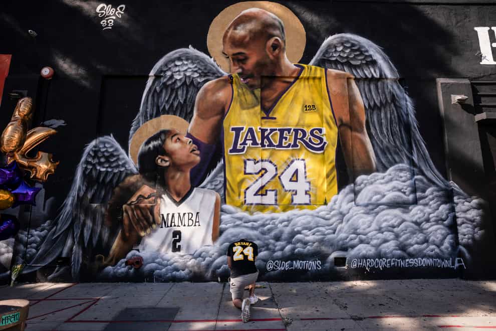 Adam Dergazarian, bottom centre, pays his respect for Kobe Bryant and his daughter, Gianna, in front of a mural painted by artist Louie Sloe Palsino (Jae C. Hong/AP)