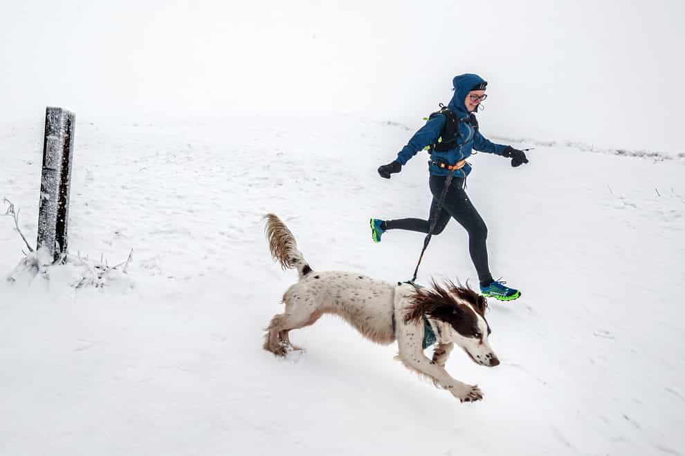 A woman runs with a dog through snow near Buxton in Derbyshire
