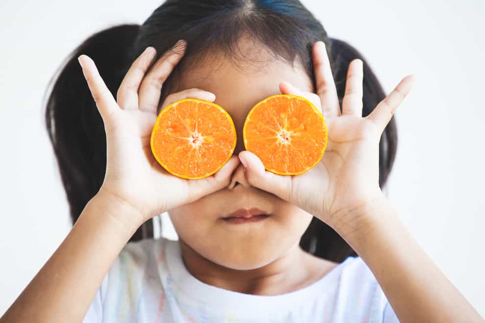 Girl holding fresh oranges covering her eyes.