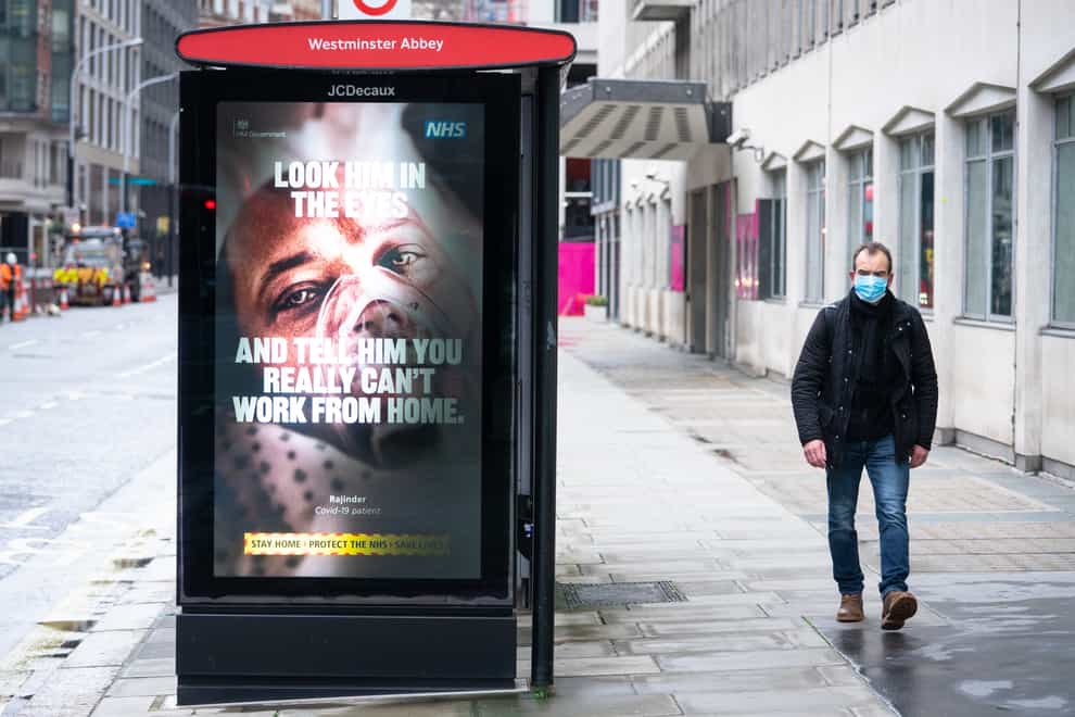 A man passes a government coronavirus advert in a bus shelter
