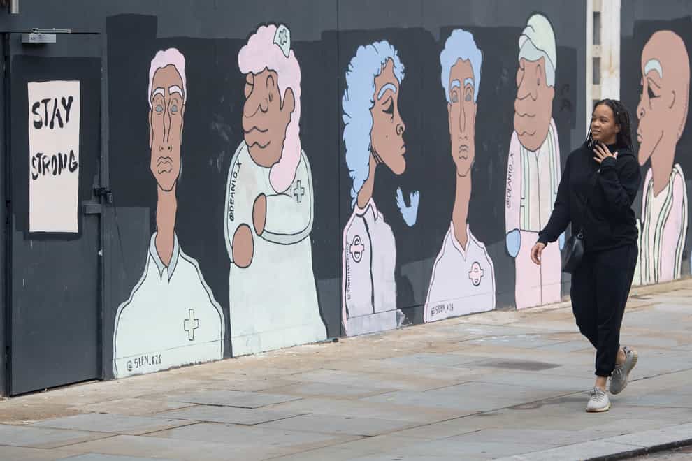 A woman passes a mural depicting BAME medical, transport and construction workers