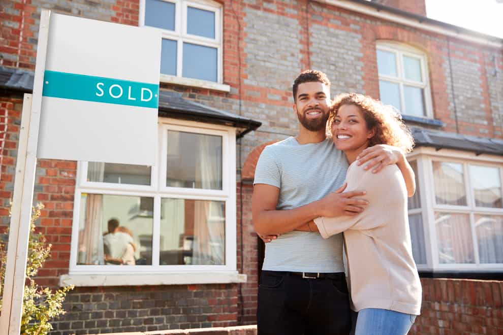 Happy couple hugging outside their new home with a 'sold' sign