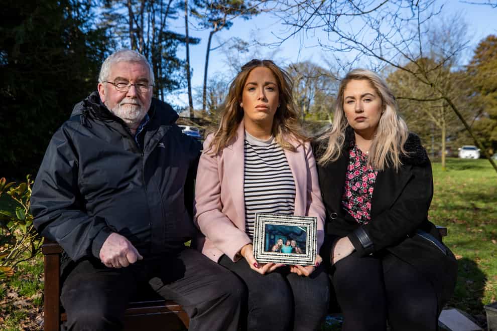 Lisa Dorrian’s father John and her sisters Michelle (centre) and Joanne (right) sitting a memorial bench to Lisa at Castle Park in Bangor beside a cherry blossom tree planted by her friends 16 years ago (Liam McBurney/PA)