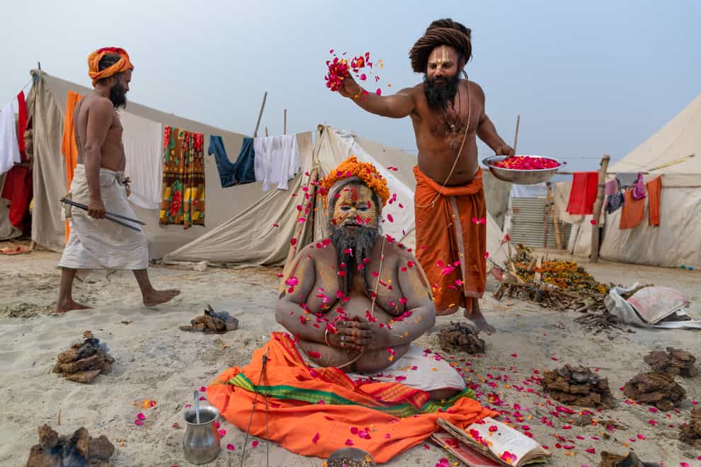 A Hindu Holy man prays as others shower flower petals on him