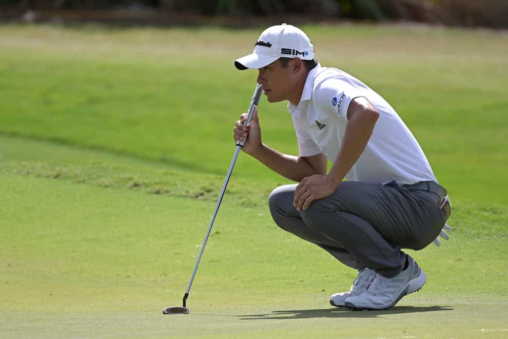 Collin Morikawa crouches while holding his putter
