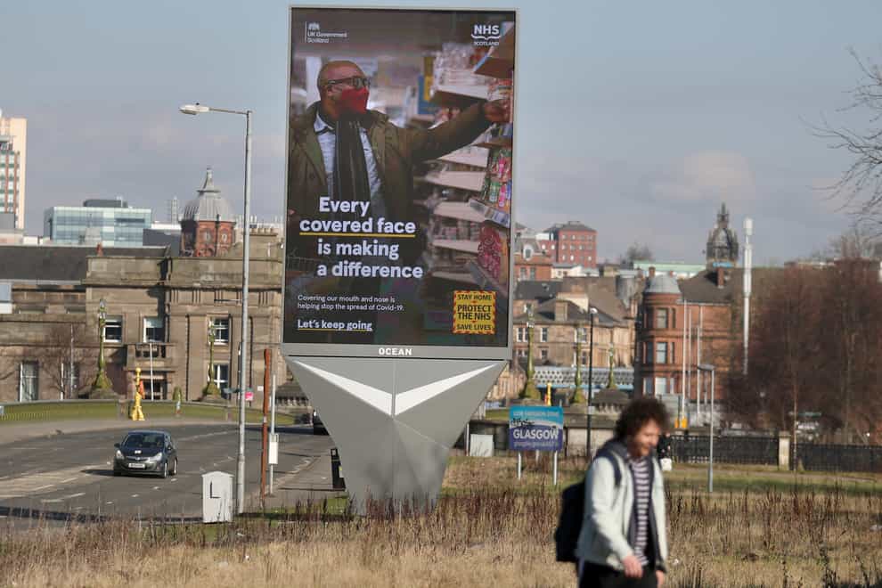 People pass an advertising board in Glasgow featuring coronavirus-related messages (Andrew Milligan/PA)