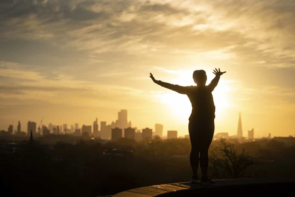 A woman performs yoga stretches as the sun rises over London