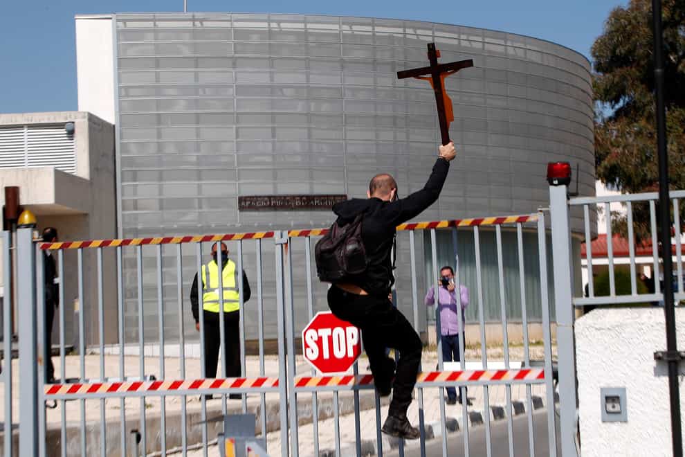 A protestor holding a cross climbs a gate outside Cyprus’s national broadcasting building