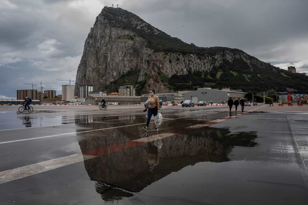 People cross the Gibraltar airport runway towards the border crossing with Spain, backdropped by the Gibraltar Rock, in Gibraltar