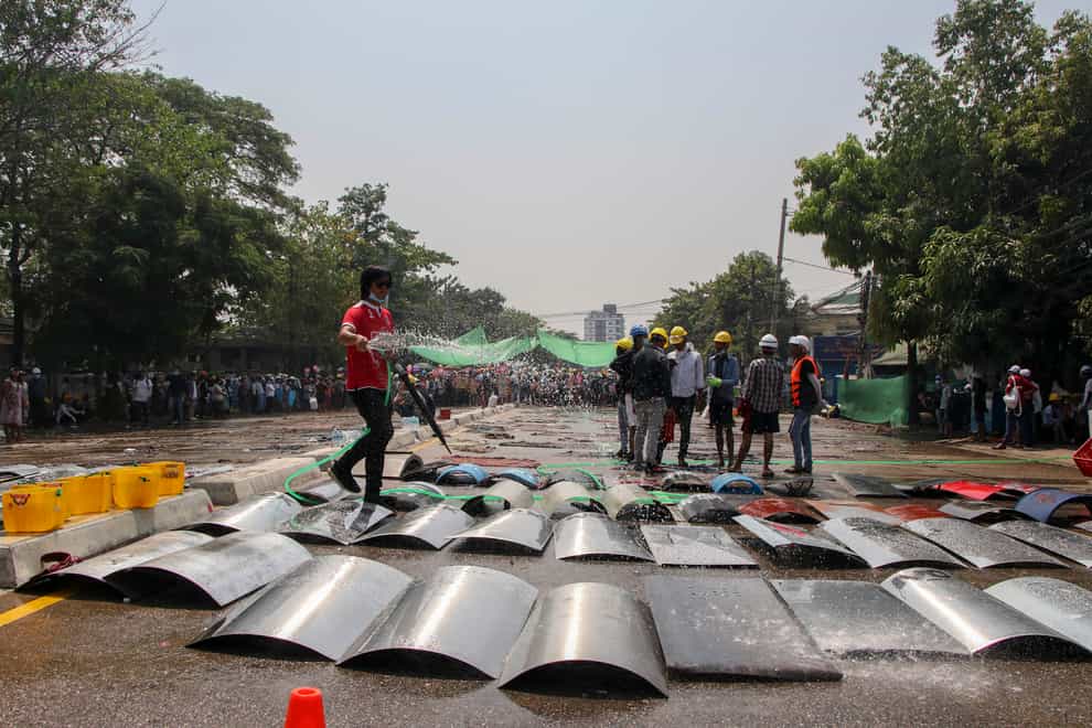 An anti-coup protester sprays water on metal-makeshift shields to prevent from heat in hot-sunny weather in Yangon, Myanmar (AP)
