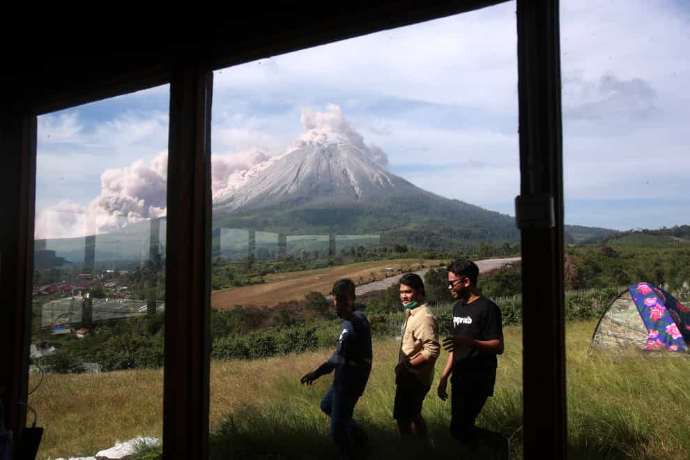 People walk past by as Mount Sinabung spews volcanic material (Binsar Bakkara/AP)