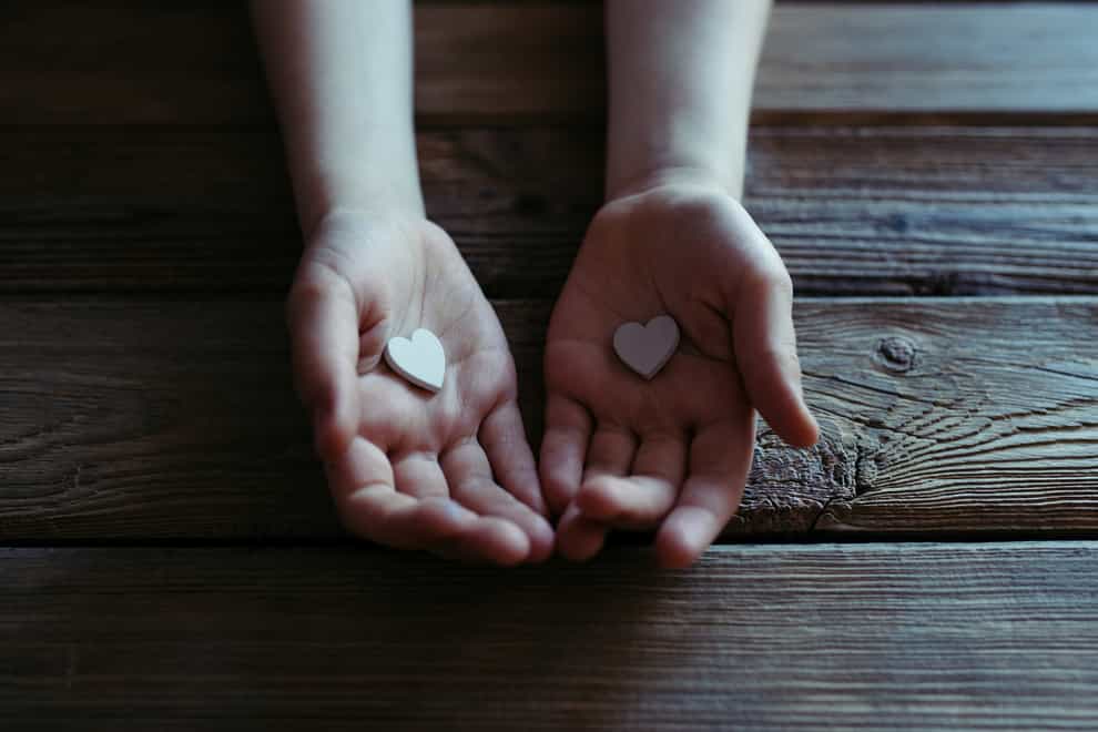 Child holding white hearts in hands over a wooden table.