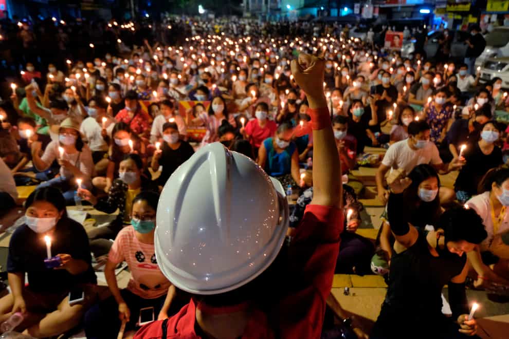 A protester raises their fist in front of a large seated crowd who are all holding candles