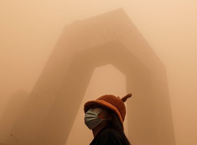 A woman wearing a face mask to help curb the spread of the coronavirus stands against the China Central Television (CCTV) building amid a sandstorm