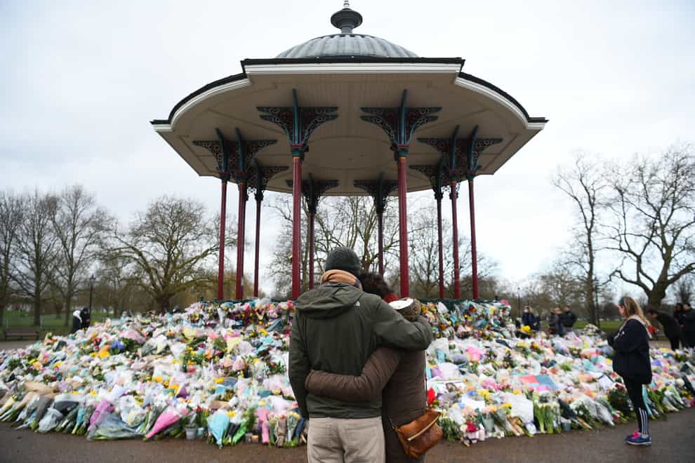 People stand next to floral tributes left at the band stand in Clapham Common, London
