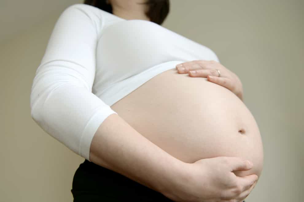A woman seven months into her pregnancy holds her stomach (Andrew Matthews/PA)