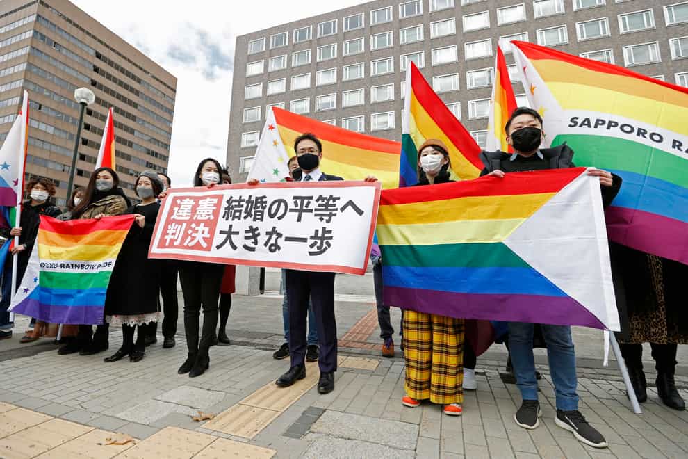 Plaintiffs’ lawyers and supporters hold rainbow flags and a banner outside a court building